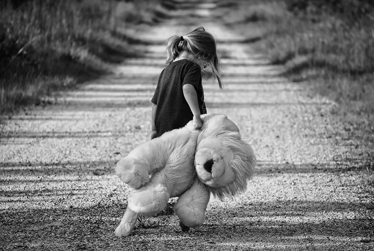 Une petite fille seule et triste tient son doudou en marchant le long de la route.
